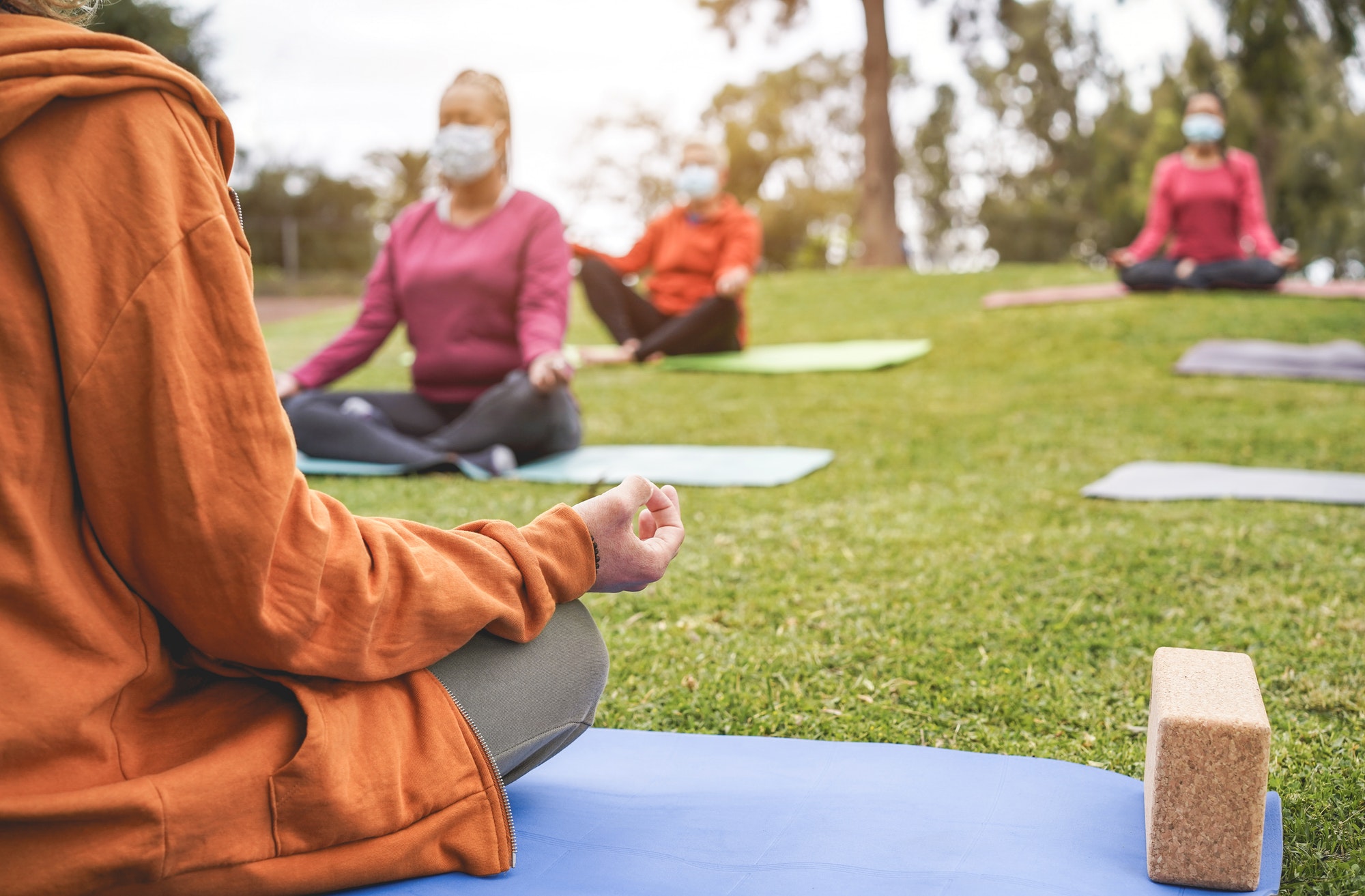People doing yoga class outdoor sitting on grass while wearing safesty masks